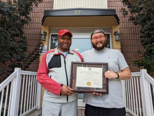 Jon et Theo, agent de développement communautaire de Salus, prenant la pose avec le diplôme d’études secondaires de Jon.